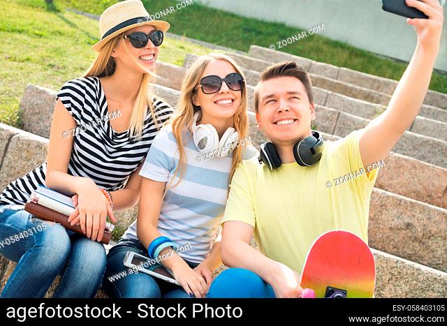 Three young happy people sitting outdoors and making selfie