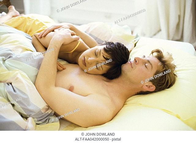 Couple asleep in bed, woman's head resting on man's chest