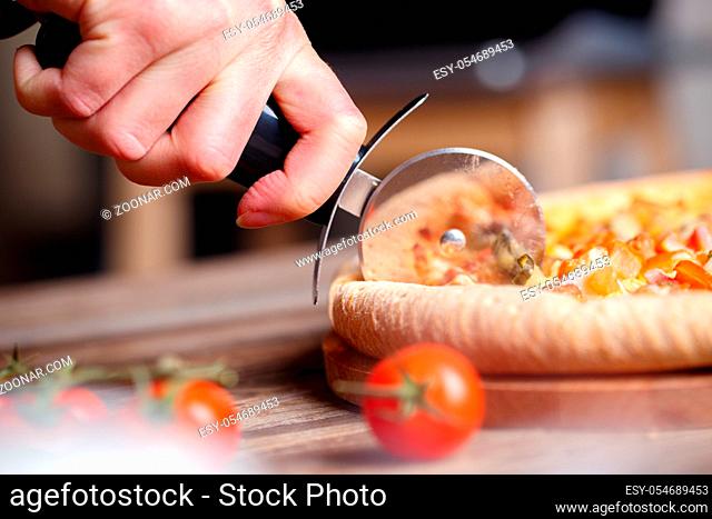 Slicing fresh pizza with pizza knife. Shallow dof. Focused on hand
