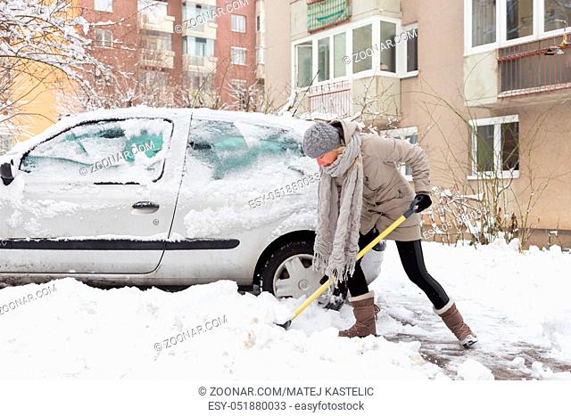 Independent woman shoveling her parking lot after a winter snowstorm