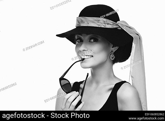 Beautiful young woman looking like Audrey Hepburn in hat with scarf and holding sunglasses