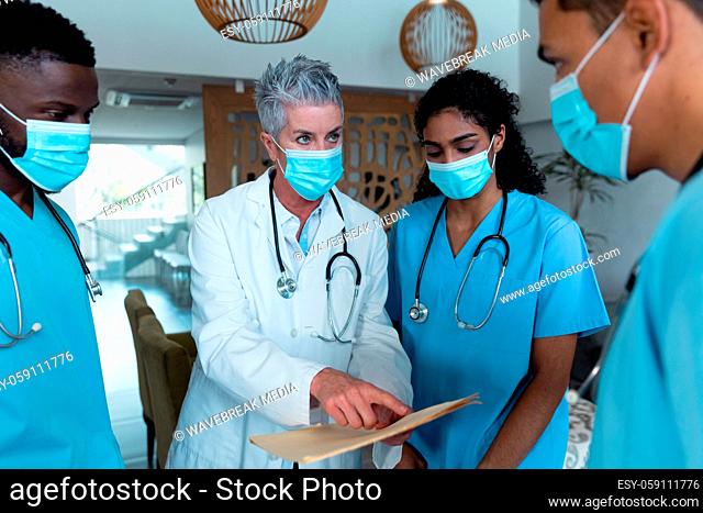 Caucasian female senior doctor and diverse hospital colleagues wearing face masks talking at meeting