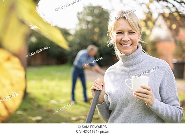 Portrait smiling, confident mature woman drinking coffee and raking autumn leaves in backyard