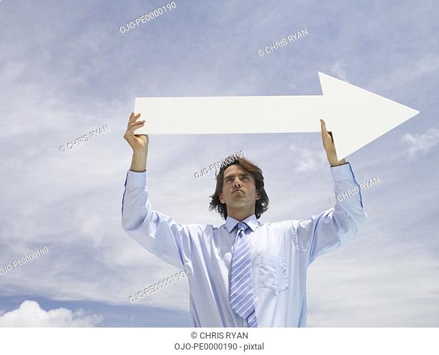 Businessman outdoors holding blank arrow with sky in background