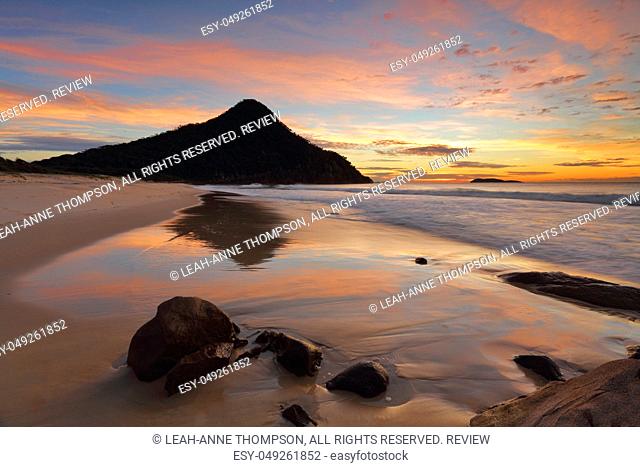 Zenith Beach and reflections in the shorebreak  Mt Tomaree and Boondelbah island in silhouette against the beautiful dawn sunrise light illuminating the sky