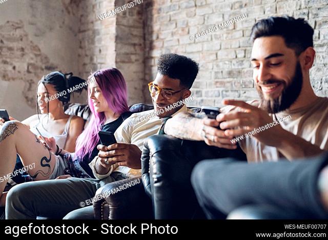 Group of friends sitting on sofa in a loft using smartphones