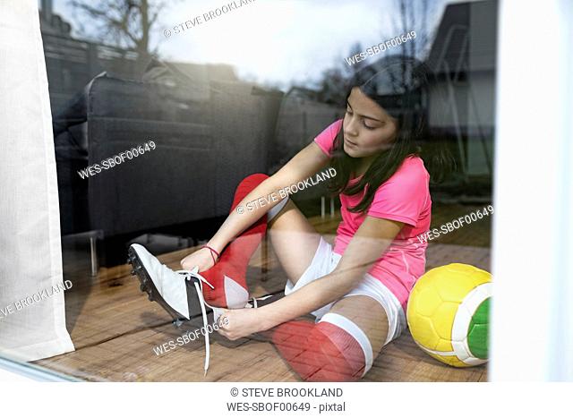 Girl putting on soccer shoes in front of living room window