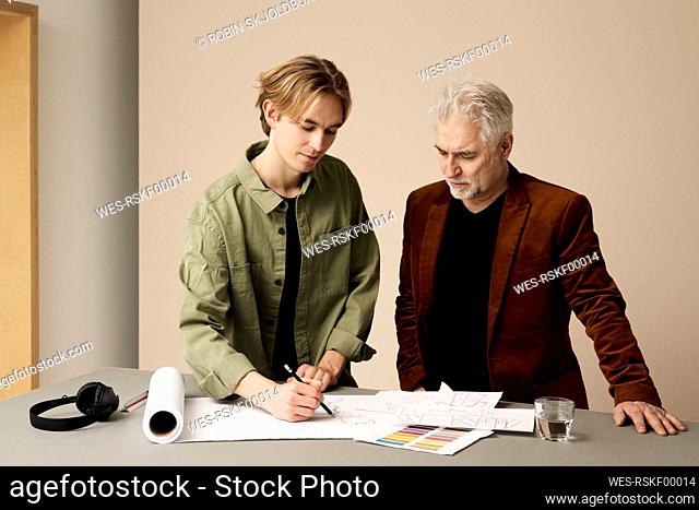 Young creative professional sketching on paper with colleague standing at table