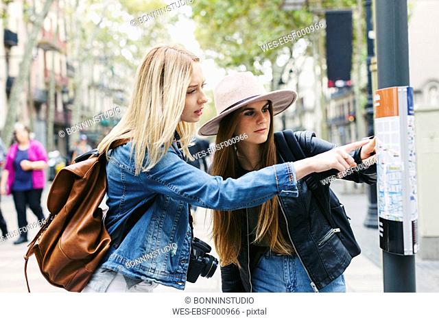 Spain, Barcelona, two young women looking at city map on pole