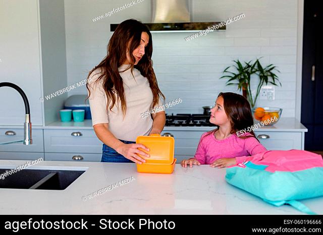 Happy caucasian mother and daughter preparing lunchbox to school in kitchen