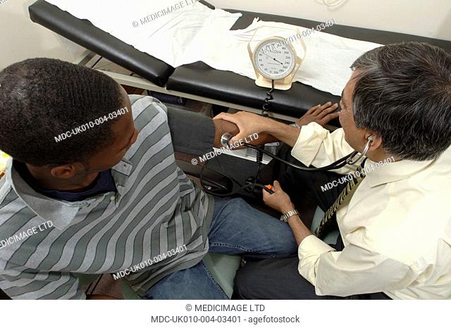 A GP checks a the blood pressure, of his patient, using a sphygmomanometer, whist listening to the blood in the artieries and veins with a stethoscope