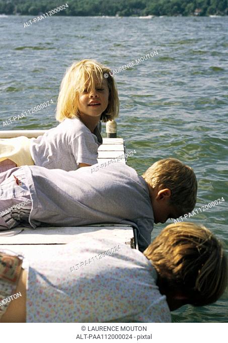 Two girls and boy lying on a wooden dock