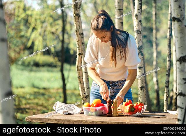 Woman makes vegetable salad outdoor at picnic in sunny day