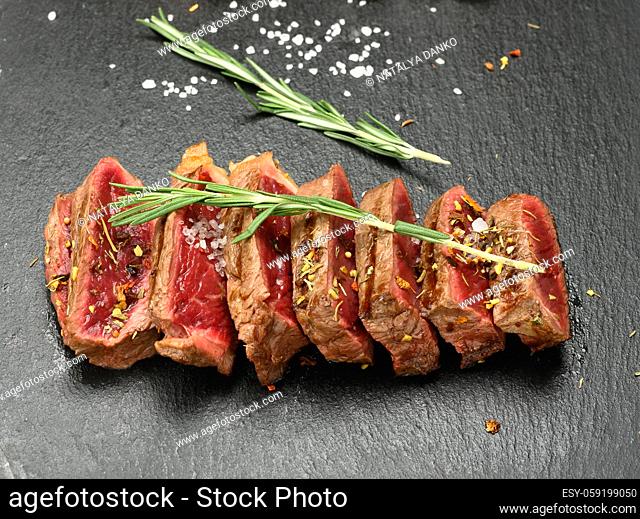fried beef steaks cut into pieces on a black board, the degree of doneness rare with blood, close up