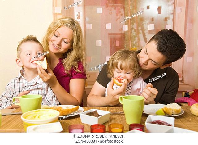 Junges Ehepaar mit zwei Kindern auf dem Schoss frühstückt gemeinsam