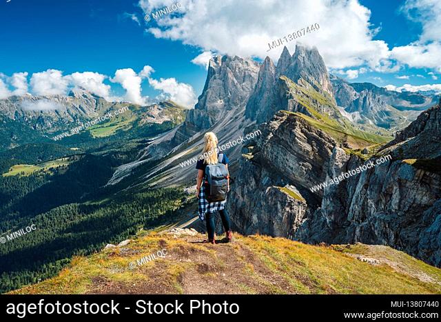 Adult women with backpack enjoy landscape of Seceda peak in Dolomites Alps, Odle mountain range, South Tyrol, Italy, Europe. Travel vacation concept