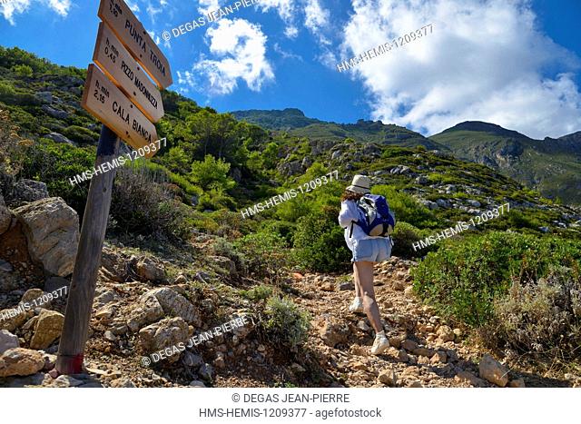 Italy, Sicily, Egadi islands, island of Marettimo, hiking trail that crosses the island, hiker with backpack and wearing a hat passing a road sign wood