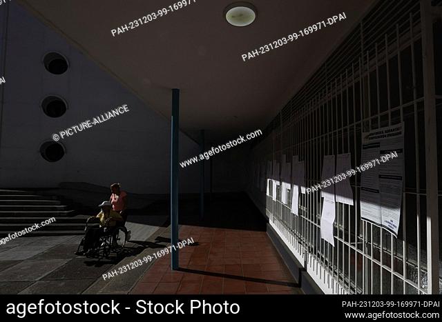 03 December 2023, Venezuela, Caracas: A man in a wheelchair and a woman leave a polling station after exercising their right to vote during the referendum on...