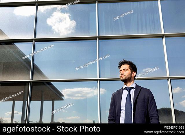 Mid adult businessman standing with eyes closed in front of office building