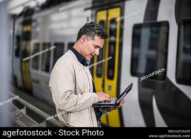 Mature businessman using tablet PC in front of train at railroad station