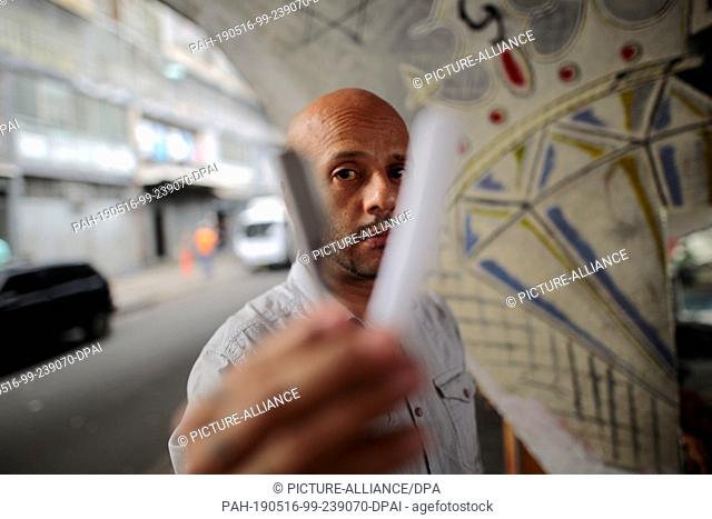 13 May 2019, Venezuela, Caracas: Jose Joserondon, hairdresser, looks through his hairdressing scissors in his ""hairdressing salon"" on the street