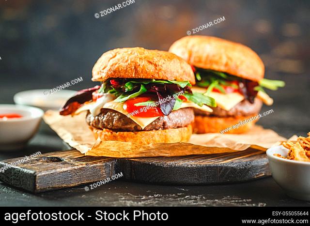Two delicious homemade burger with beef, tomatoes, cheese, arugula and chard on a wooden cutting board. Street food, fast food
