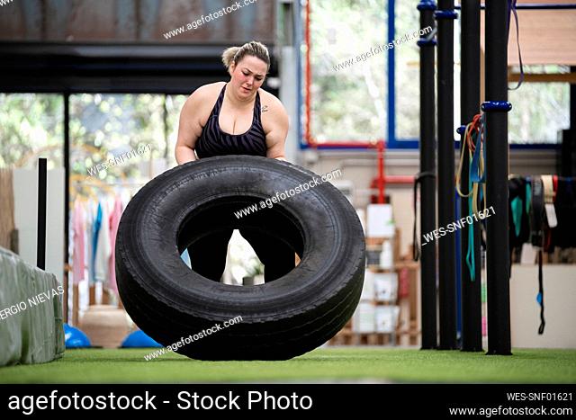 Determined young woman working out with tire in gym