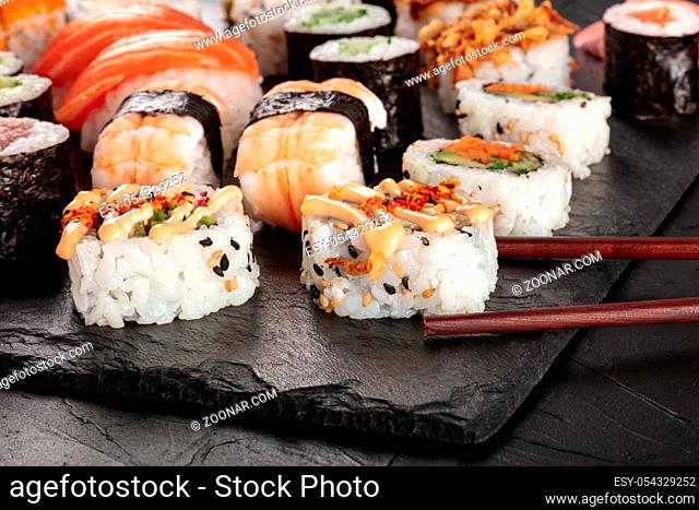 Large sushi set, close-up with chopsticks on a black background. An assortment of various maki, nigiri and rolls