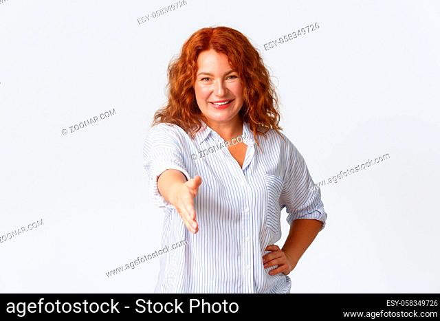 Confident smiling middle-aged redhead female entrepreneur, businesswoman extend hand for handshake, greeting business partner