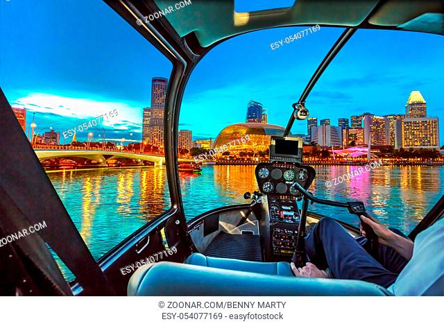 Helicopter cockpit interior flying on Skyline of Singapore in marina bay with cruise boats in the harbor at blue hour. Night scene waterfront in Singapore bay