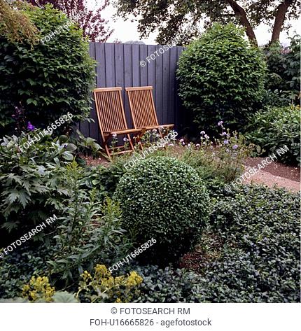 Wooden chairs against fence in country garden with clipped shrubs