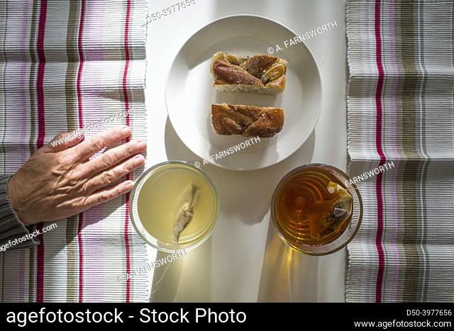 Two cups of tea on a table and two pieces of cake on a plate and a woman's hand