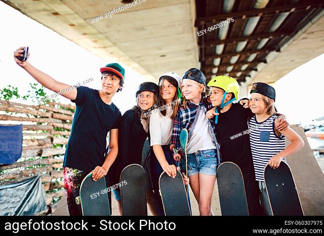 large group friends children skateboarders make videos, online broadcasts, video calls on phone in skate park. Kids spend time on skateboarding training