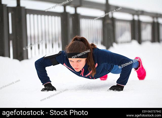 Fitness girl doing pushups on work out fitness at snow winter park, telephoto