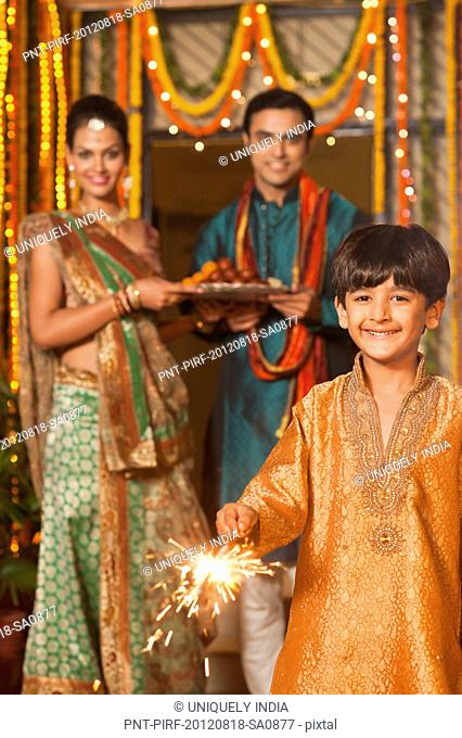 Boy burning fire crackers with his parents in the background on Diwali