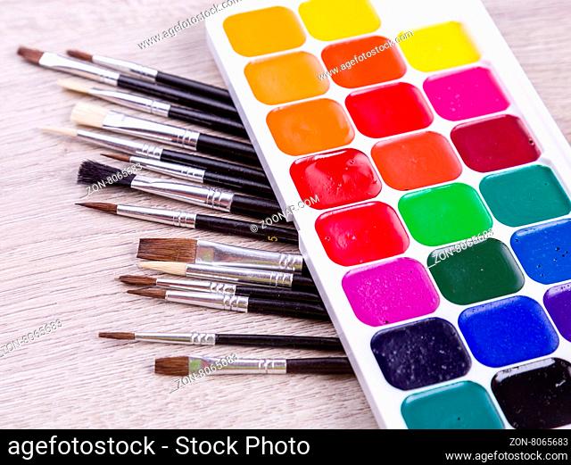 Watercolor paints with set of paint brushes on wooden background