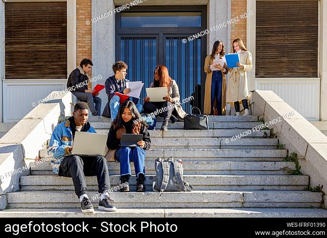 Friends studying over tablet PC and laptop on steps on campus