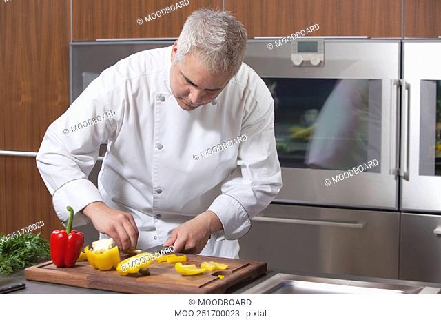 Mid- adult chef slices red and yellow bell peppers