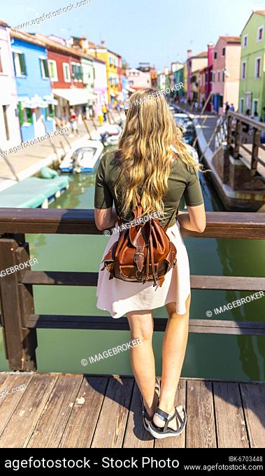 Young woman in front of colorful houses, canal with boats and colorful house facades, Burano Island, Venice, Veneto, Italy, Europe