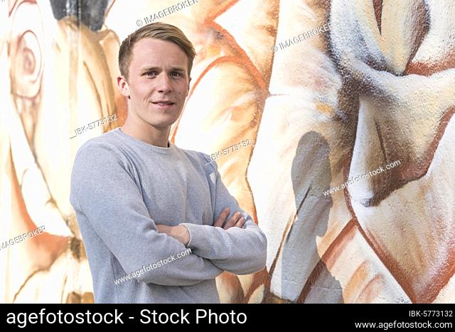 Young man in front of graffiti wall, Munich, Bavaria, Upper Bavaria, Germany, Europe