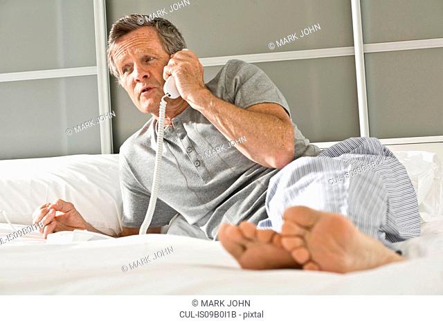Senior man reclining on bed talking on landline telephone