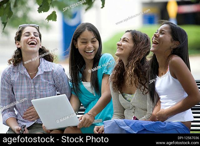 Four teenage girls sitting on a bench and smiling in the school campus