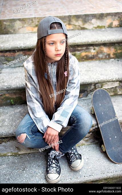 child girl sit on concrete stairs with skateboard
