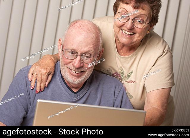 Smiling senior adult couple having fun on the computer laptop together