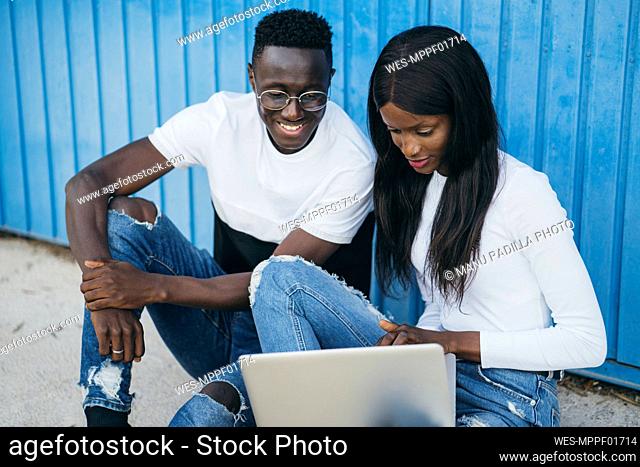 Woman using laptop while sitting with boyfriend near blue wall