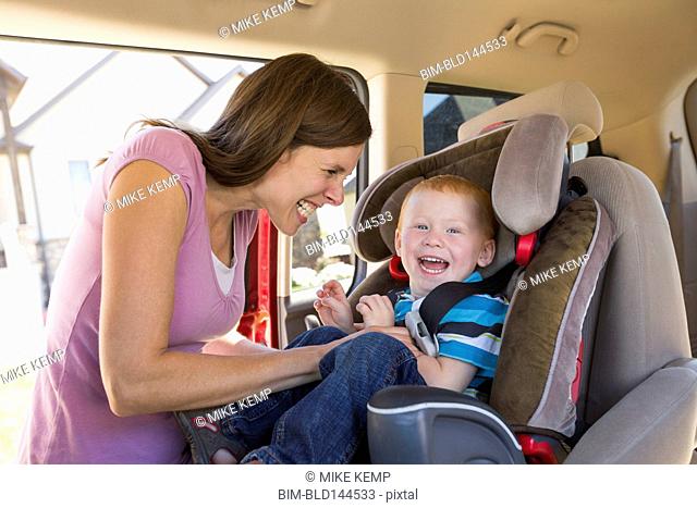 Caucasian mother fastening son into car seat