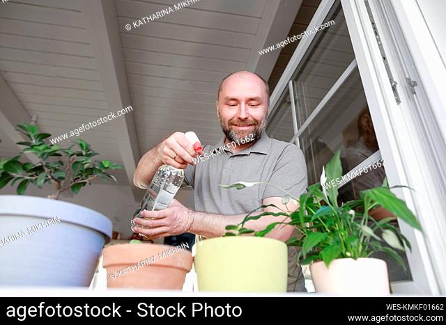 Mature man spraying water on potted plants in house