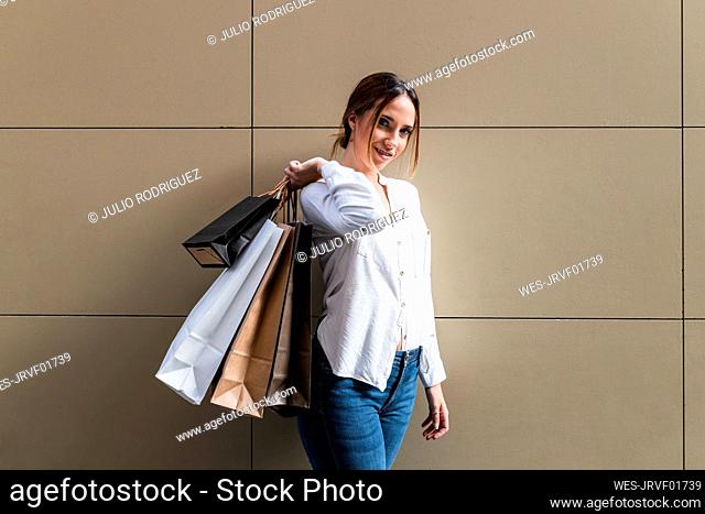 Young woman carrying shopping bags while standing near wall
