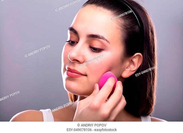 Beautiful Young Woman Applying Makeup Using Pink Blender Sponge