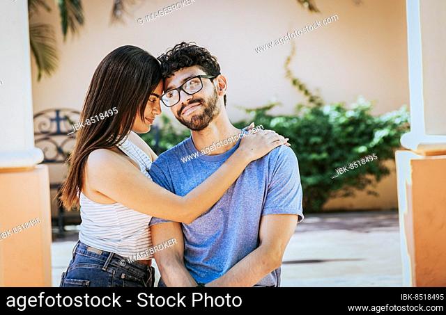 Attractive girl tenderly hugging her boyfriend outdoors. Girl hugging her boyfriend while he smiles at her, Happy couple, Girl hugging her boyfriend outside